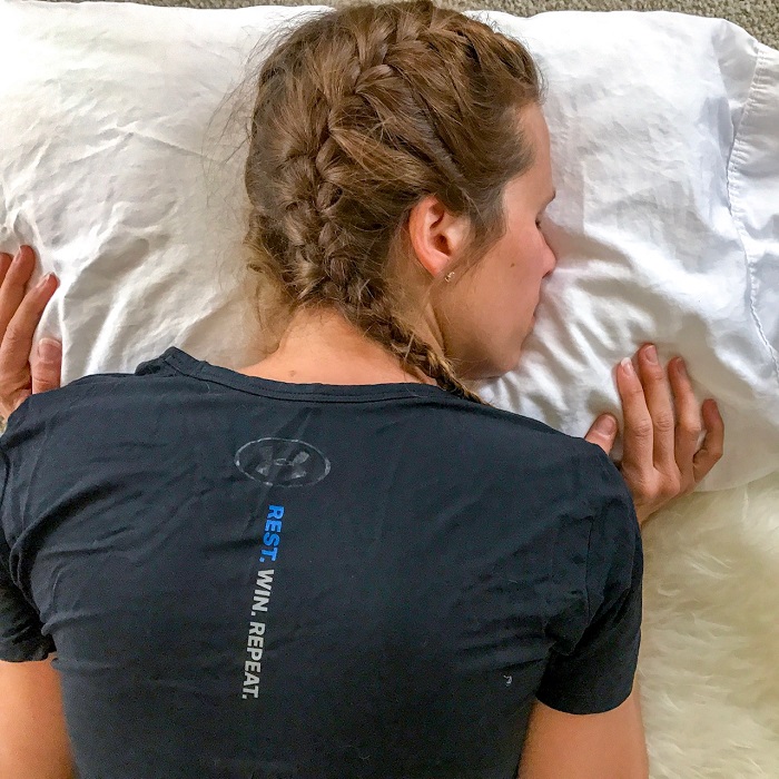 A woman sleeping in a black shirt with braids. Sleep is a great recovery method.