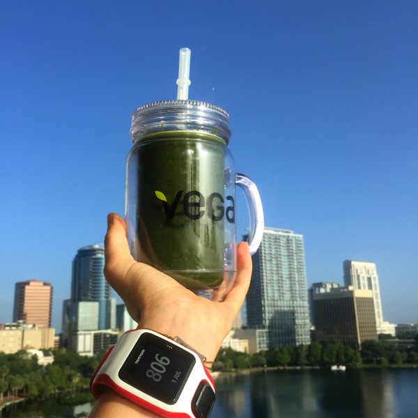 A person holding up a green smoothie in front of a city.